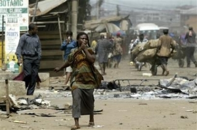 People walk pass burnt dead bodies on the ground in a street in Onitsha, Nigeria,Thursday, Feb. 23, 2006. Gangs of rioters armed with machetes and shotguns poured through the streets of the mainly Christian southern city of Onitsha on Wednesday as the dea