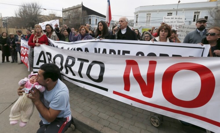 A demonstrator kisses his child as archbishop Gonzalo Duarte prays outside Congress during a rally against the draft law of the Chilean government which seeks to legalize abortion, in Valparaiso, August 4, 2015. President Michelle Bachelet's push to relax strict abortion laws in socially conservative Chile has created a rift inside her ruling coalition and key elements of the reform are likely to be scratched. Bachelet's proposals would allow an abortion if a mother's life is in danger, if a baby is deemed to have 'defects' or when a pregnancy is a result of rape. The banner reads: 'Abort No.'