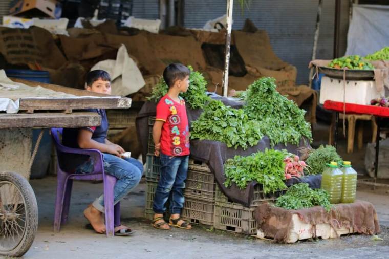 Boys stand near a vegetable stand inside a market in the rebel-held al-Shaar neighbourhood of Aleppo, Syria, September 17, 2016.