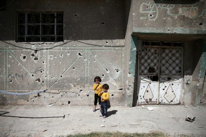 Children stand in front of the bullet-riddled facade of a building in the rebel-held Douma neighbourhood of Damascus, Syria September 25, 2016.