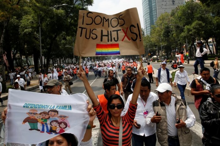 A woman holds a sign near the Angel of Independence monument in support for the legalization of gay marriage while others behind participate in a protest march against it and defend their interpretation of traditional family values, in Mexico City, Mexico September 24, 2016. The sign reads: 'We are your Children.'