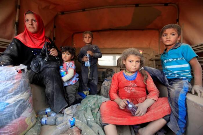 Displaced people who are fleeing from clashes sit at a military vehicle in Qayyarah, during an operation to attack Islamic State militants in Mosul, Iraq.