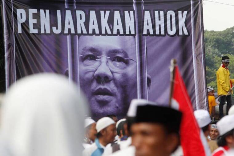 Members of hardline Muslim groups stand around a poster during protest against Jakarta's incumbent governor Basuki Tjahaja Purnama. The poster reads 'Ahok should be jailed.'