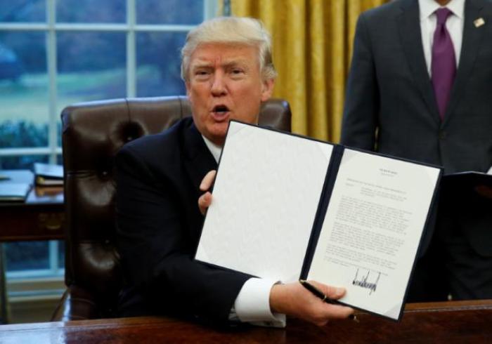 President Donald Trump holds up the executive order on withdrawal from the Trans Pacific Partnership after signing it in the Oval Office of the White House in Washington January 23, 2017.