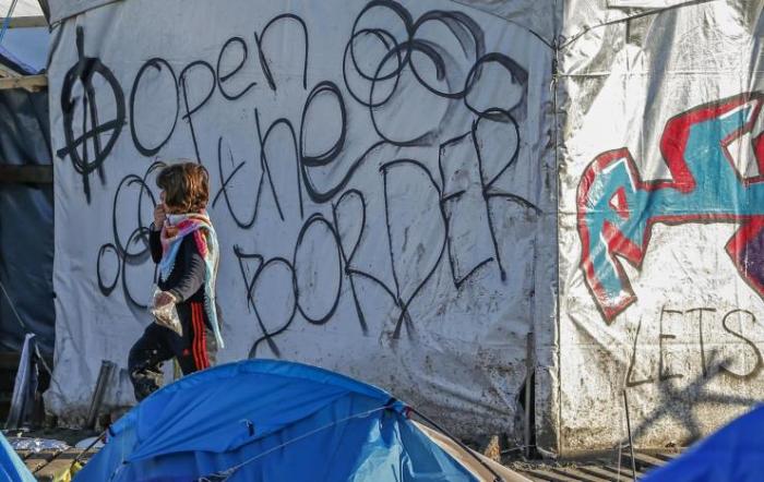 A young migrant walks past graffiti reading 'Open the border' in a muddy field at a camp of makeshift shelters for migrants and asylum-seekers from Iraq, Kurdistan, Iran and Syria, called the Grande Synthe jungle, near Dunkirk, France, January 25, 2016. RE