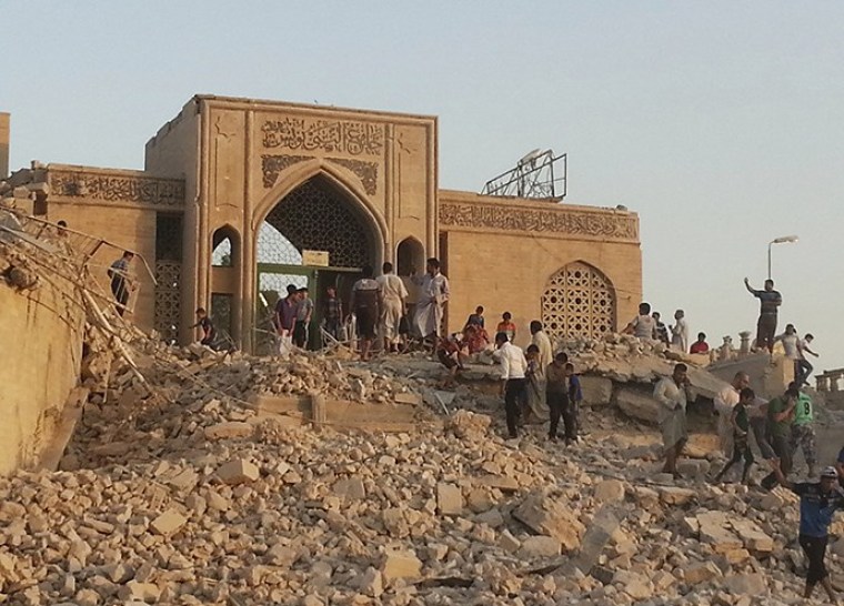 People walk through the rubble of the Prophet Younis Mosque after it was destroyed in a bomb attack by militants of the Islamic State, formerly known as the Islamic State in Iraq and the Levant (ISIL), in the city of Mosul, July 24, 2014.