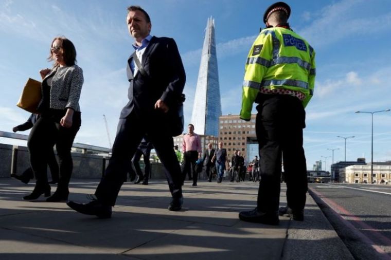 Commuters walk past a City of London police officer standing on London Bridge after is was reopened following an attack which left 7 people dead and dozens of injured in central London, Britain, June 5, 2017.