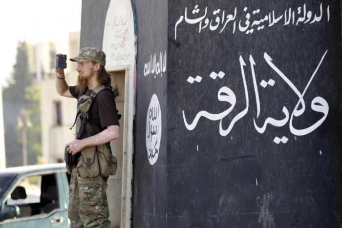 A militant Islamist fighter uses a mobile phone to film his fellow fighters taking part in a military parade along the streets of Syria's northern Raqqa province, June 30, 2014. The terrorist group has recently called on its supporters to kill more civilians during the Ramadan.