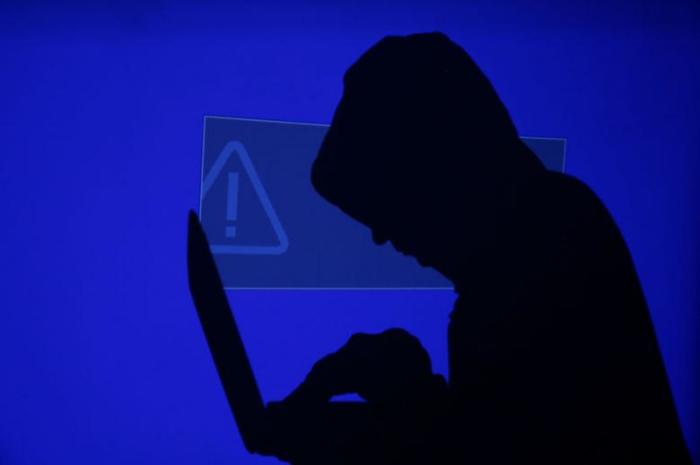 A hooded man holds a laptop computer as blue screen with an exclamation mark is projected on him in this illustration picture taken on May 13, 2017.