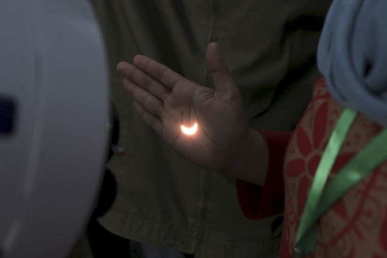 Light from a solar eclipse is refracted through a telescope and cast on to a person's hand on the Ampera Bridge over the Musi River in Palembang, South Sumatra province, Indonesia.