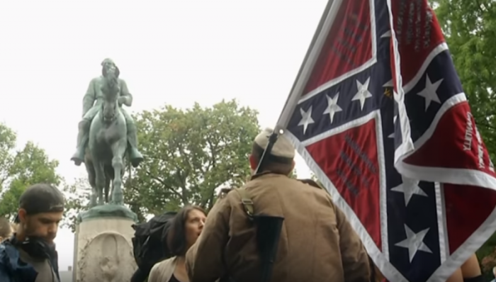 Former Pensacola Christian College student Allen Armentrout stands in Confederate uniform waving the Confederate battle flag in front of a statue of Robert E. Lee in Charlottesville, Virginia.