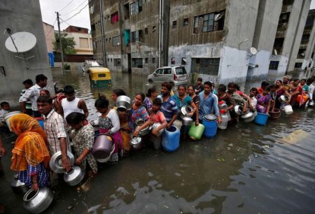 People wait in a line to collect drinking water from a municipal tanker at a flooded residential colony in Ahmedabad, India in August 2017.