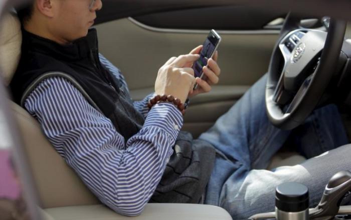 Credit : A man texts on his mobile phone in a car in Beijing, China, April 3, 2015.