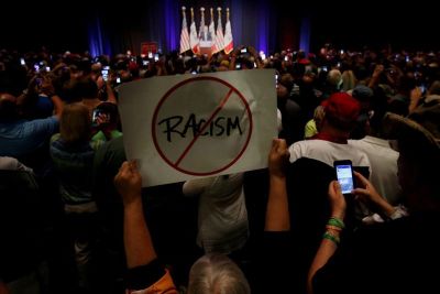 A protester holds up an anti-racism sign as Republican presidential nominee Donald Trump speaks during a campaign rally in Cedar Rapids, Iowa, U.S., July 28, 2016.