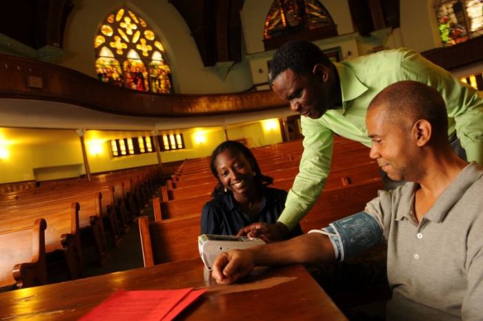 Dr. Gbenga Ogedegbe (standing), director of the Division of Health and Behavior in the Department of Population Health, visits a church in Harlem, where he demonstrates the proper technique for taking blood pressure readings.