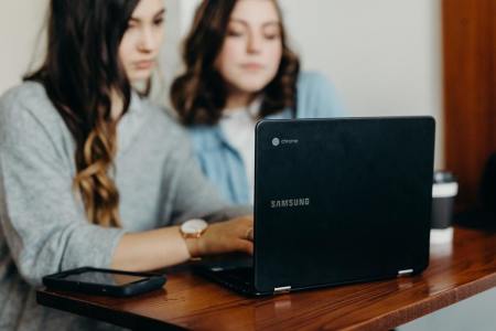 Two girls sit in front of a laptop. 