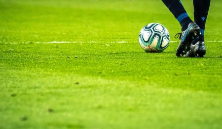 A soccer player stands near a ball on a grassy field.