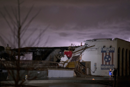 A television news crew works in front of a mural on heavily damaged The Basement East in the East Nashville neighborhood as lightning strikes in the background on March 3, 2020 in Nashville, Tennessee. 