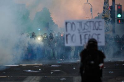 Smoke rises near a demonstrator holding a sign and facing a row of police near the 5th police precinct during a demonstration to call for justice for George Floyd, a black man who died while in custody of the Minneapolis police, on May 30, 2020, in Minneapolis, Minnesota. Clashes broke out and major cities imposed curfews as America began another night of unrest Saturday.