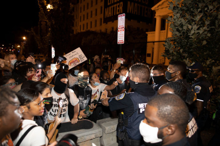 Washington D.C. Police try to keep demonstrators back as they gather at Black Lives Matter plaza on August 27, 2020, in Washington, D.C. Protesters gathered on the final night of the Republican National Convention in which both President Donald Trump Vice President Mike Pence accepted the Republican nomination as candidates for a second term. One demonstrator is seen wearing a Black Trans Lives Matter T-shirt and another in the background is holding a sign saying 'Burn Down the Police Station.'