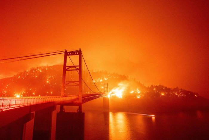 A boat motors by as the Bidwell Bar Bridge is surrounded by fire in Lake Oroville during the Bear fire in Oroville, California on September 9, 2020. - Dangerous dry winds whipped up California's record-breaking wildfires and ignited new blazes Tuesday, as hundreds were evacuated by helicopter and tens of thousands were plunged into darkness by power outages across the western United States.