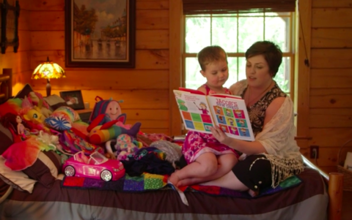 Phoenix, a four-year-old subject of the HBO documentary 'Transhood,' sits on his bed wearing a dress as his mother reads him a story called 'Jacob's New Dress.'