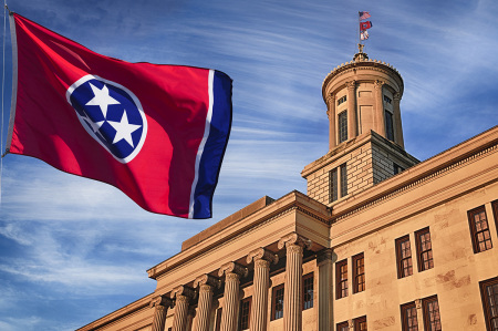 Tennessee state Capitol building front exterior in Nashville, with wind blowing the U.S. state flag outside on a partly cloudy day.