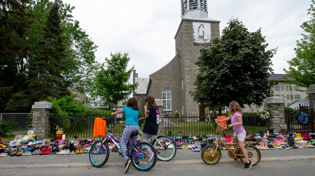 Local children of Kahnawake, Quebec, stop on May 30, 2021, to view the hundreds of children's shoes placed in front of the St. Francis Xavier Church as members of the community of the Kahnawake Mohawk Territory, Quebec, commemorate the news that a mass grave of 215 Indigenous children was found at the Kamloops Residential School in British Columbia, Canada.