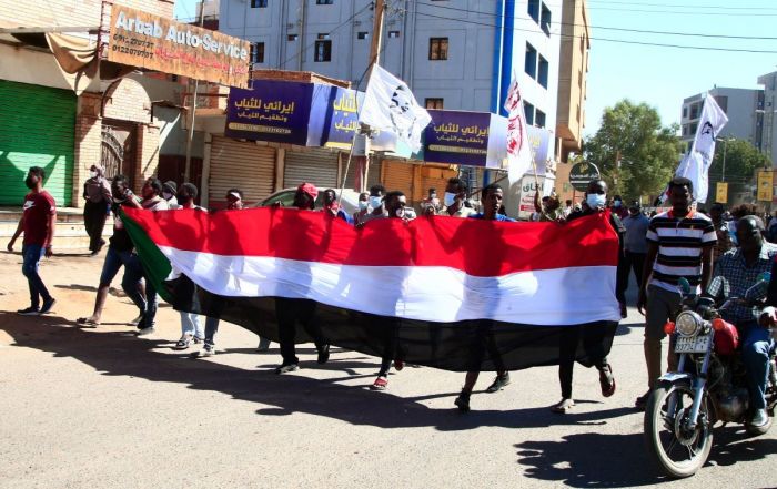 Sudanese demonstrators carry a large national flag as they take to the streets of the capital Khartoum as tens of thousands protest against the army’s October 25 coup on December 30, 2021. 