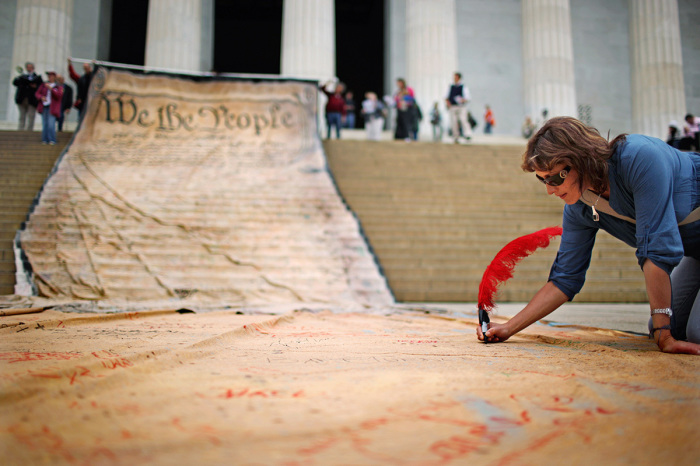 A woman signs a giant banner printed with the Preamble to the United States Constitution during a demonstration against the Supreme Court's Citizens United ruling at the Lincoln Memorial on the National Mall October 20, 2010, in Washington, D.C. The rally at the memorial was organized by brothers Laird and Robin Monahan, who spent the last five months walking from San Francisco, California, to Washington to protest the court decision, which overturned the provision of the McCain-Feingold law barring corporations and unions from paying for political ads made independently of candidate campaigns. 