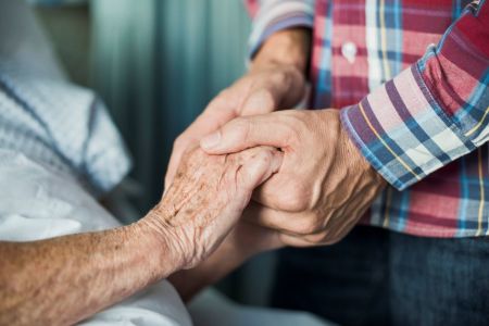 Close up of son holding his mothers hands in hospital.