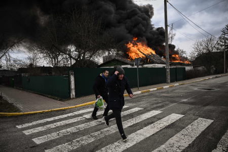 People run for cover in front of a burning house during shelling in the city of Irpin, outside Kyiv, on March 4, 2022. More than 1.2 million people have left Ukraine into neighbouring countries since Russia launched its full-scale invasion on February 24, United Nations figures showed on March 4, 2022. 