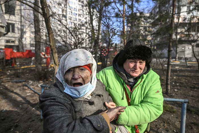 A woman is evacuated from a burning apartment building in Kyiv on March 15, 2022, after strikes on residential areas killed at least two people, Ukraine emergency services said as Russian troops intensified their attacks on the Ukrainian capital. - A series of powerful explosions rocked residential districts of Kyiv early today killing two people, just hours before talks between Ukraine and Russia were set to resume. 