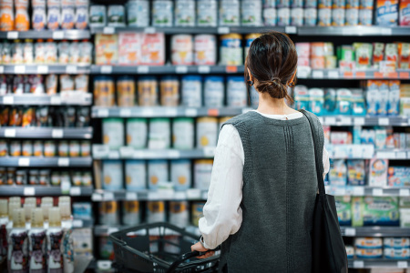 Rear view of young Asian mother with a shopping cart grocery shopping for baby products in a supermarket. 