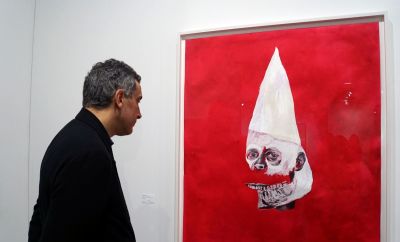 A visitor watches the work of US artist Wardell Milan, 'Amerika: Klansman, David' (2019), representing a deconstructed face with a KKK hood, during a preview on December 4, 2019 ahead of the opening the following day of the Art Basel international fair that takes place annually in Miami Beach the first week of December. - Climate change, pollution, racial issues and social commentary are some of the issues addressed by hundreds of artists showcased in Art Basel by more than 200 galleries from all over the world. 