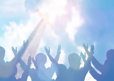 Soft focus of Christians raising their hands up to worship together in church revival meeting with an image of wooden cross over cloudy sky. 