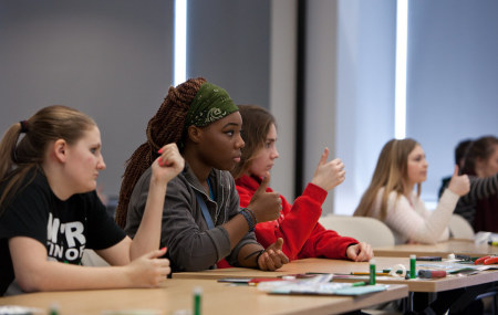 Students sit next to each other behind a large table.