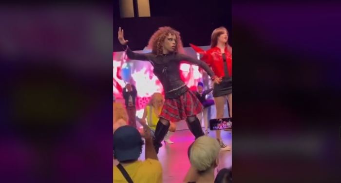 Screenshot of a video with a young boy wearing makeup and dressed in women’s clothing dancing on stage at DragCon in Los Angeles. 