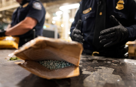 An officer from the US Customs and Border Protection, Trade and Cargo Division finds Oxycodone pills in a parcel at John F. Kennedy Airport's US Postal Service facility on June 24, 2019 in New York. - In a windowless hangar at New York's JFK airport, dozens of law enforcement officers sift through packages, looking for fentanyl -- a drug that is killing Americans every day. The U.S. Postal Service facility has become one of multiple fronts in the United States' war on opioid addiction, which kills tens of thousands of people every year and ravages communities. 