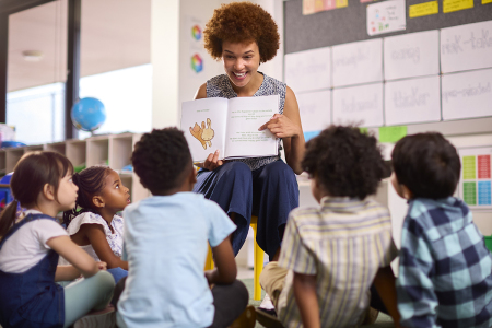 Students sit on the floor and listen to the teacher read a story.