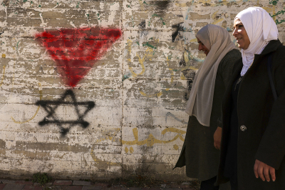 Palestinian women walk past a graffiti of the Star of David under an inverted 'red triangle,' a symbol that the Palestinian Hamas movement's military wing Al-Qassam Brigades uses to identify Israeli targets in their videos, in the West Bank city of Hebron on November 30, 2023, on the seventh day of a truce between Israel and Hamas. The warring parties have agreed a pause in fighting to allow time for the militant group to release Israeli hostages in exchange for Palestinian prisoners. 