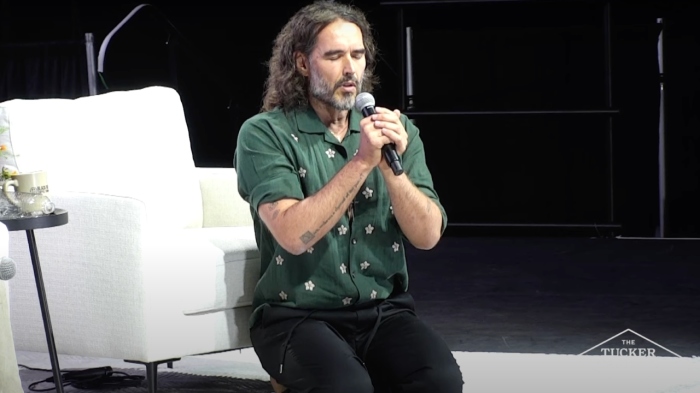 A barefoot Russell Brand kneels in prayers at the conclusion of his conversation with Tucker Carlson during at event in Phoenix, Arizona, on Sept. 4, 2024.