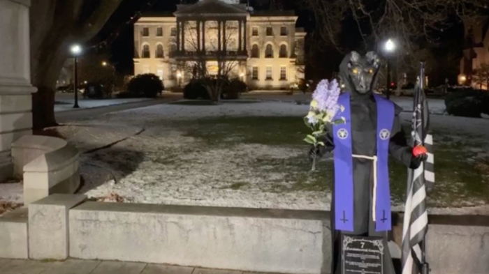 A Baphomet statue at the New Hampshire State House in Concord, New Hampshire, is adorned in a purple stole emblazoned with the inverted pentagram and goat's head of the TST logo, as well as two inverted crosses.