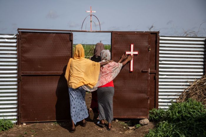 Three women touch a cross as they leave a Catholic church in Shagarab refugee camp on August 15, 2021, in Shagarab, Sudan. Situated about 70 km west of the Eritrean border, the refugee camp exist since 1968 and hosts more than 60,000 people. 