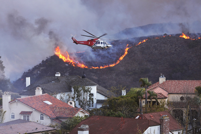 A helicopter flies over homes threatened by the wind-driven Palisades Fire in Pacific Palisades, California, Jan. 7, 2025. A fast-moving brushfire in a Los Angeles suburb burned buildings and sparked evacuations as 'life threatening' winds whipped the region. More than 200 acres (80 hectares) was burning in Pacific Palisades, a upscale spot with multi-million dollar homes in the Santa Monica Mountains, shuttering a key highway and blanketing the area with thick smoke. 