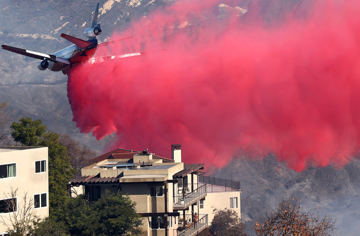 A person watches from a balcony as a firefighting aircraft drops the fire retardant Phos-Chek near homes during the Palisades Fire as wildfires cause damage and loss through Los Angeles County on Jan. 10, 2025, in Topanga, California. Multiple wildfires fueled by intense Santa Ana Winds are burning across Los Angeles County. Reportedly at least 10 people have died with over 180,000 people having been under evacuation orders. Over 9,000 structures have been damaged or burned while more than more than 25,000 acres were burning from the fires. 