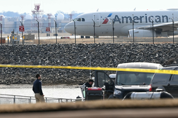 An American Airlines plane prepares to take off as investigators carry pieces of wreckage from the waters of the Potomac River after American Airlines flight 5342 on approach to Reagan National Airport crashed into the river after colliding with a U.S. Army helicopter near Washington, D.C., on Jan. 30, 2025. Recovery operations pulled 28 bodies from the river into which both crashed.