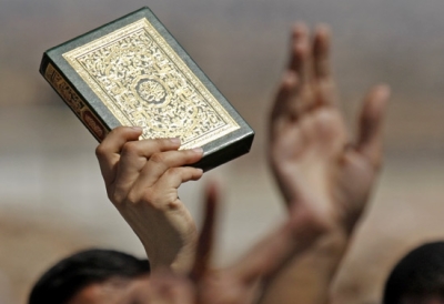 A Palestinian worshipper holds up a copy of the quran, Islam's holy book, as he crowds with others trying to reach the Al Aqsa Mosque, at the Kalandia Checkpoint between the West Bank town of Ramallah and Jerusalem, Friday, Sept. 21, 2007.