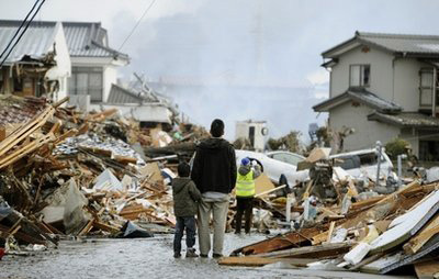 A father and child who lost their home stand in front of debris in Sendai, northern Japan Saturday, March 12, 2011 after Japan's biggest recorded earthquake slammed into its eastern coast Friday.