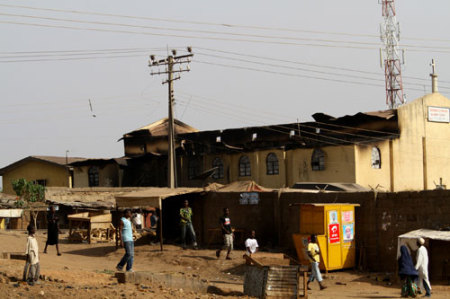 People walk past a burnt church on Ahmadu Bello way, two days after an election riot, in Kaduna metropolis in northern Nigeria April 20, 2011.